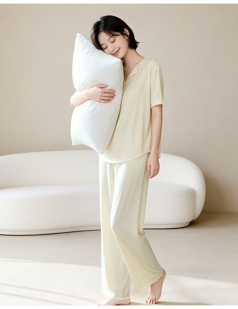 Full-body model showcase of the light yellow pajama set with a pillow beside a sofa - VEIMIA
