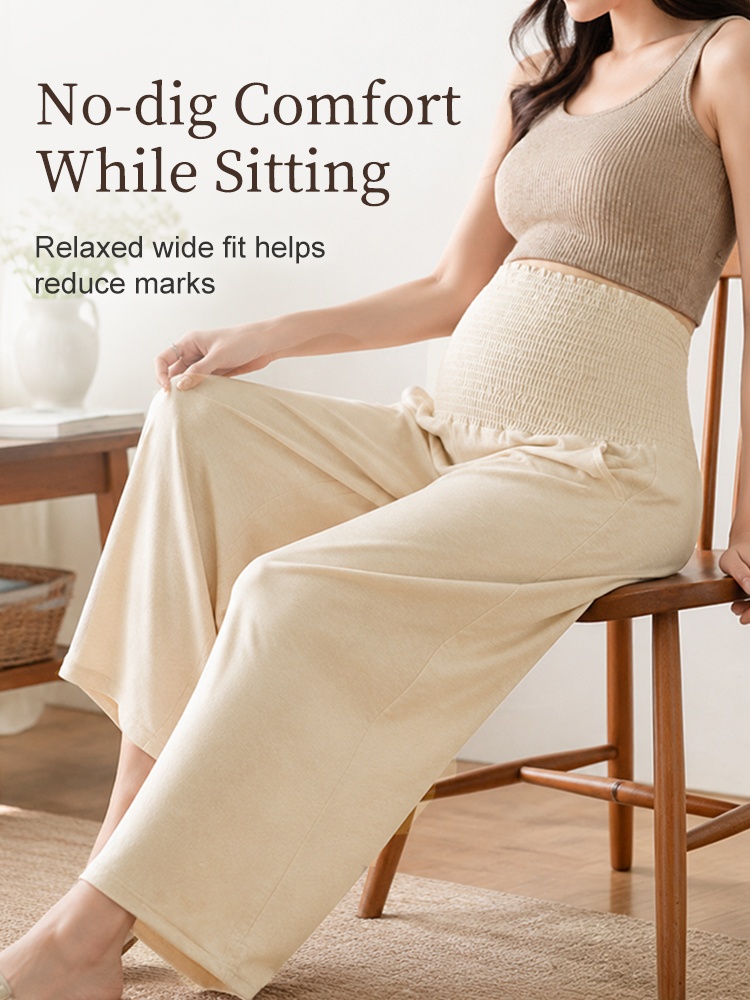 Seated pregnant model wearing relaxed beige maternity pants with wide leg fit VEIMIA