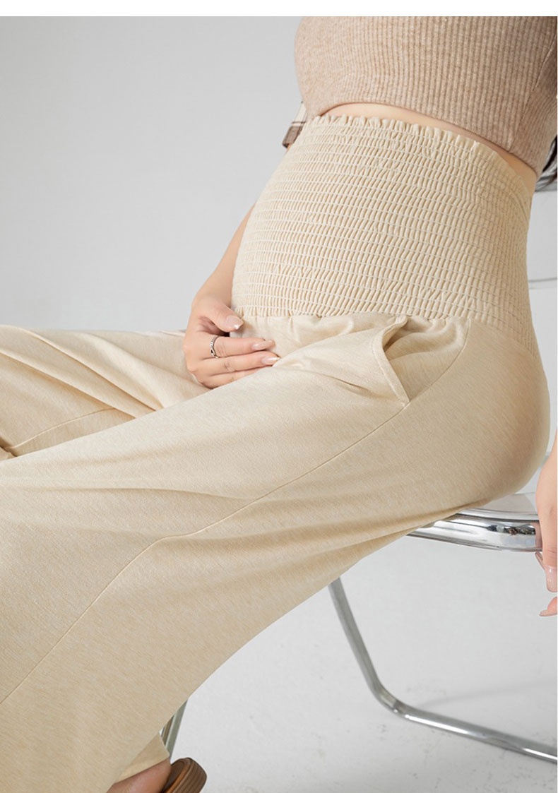 Seated model wearing beige maternity pants with high stretch belly panel VEIMIA