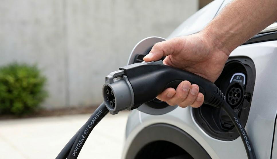 Close-up of a person's hand inserting a Type 2 portable EV charging cable into a silver car's port.