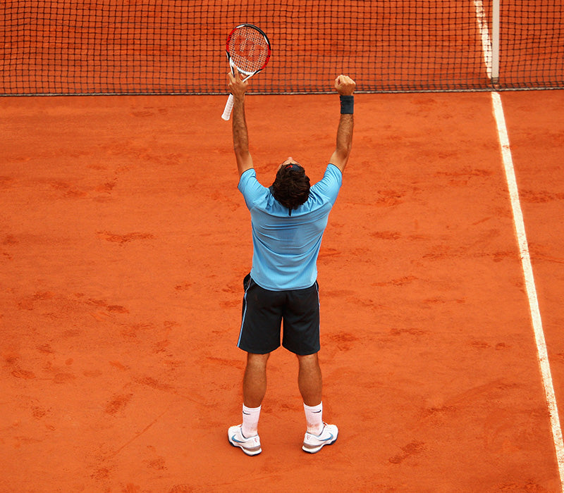 Roger Federer, back turned to the camera with hands above his head holding his racket in his left hand, celebrating