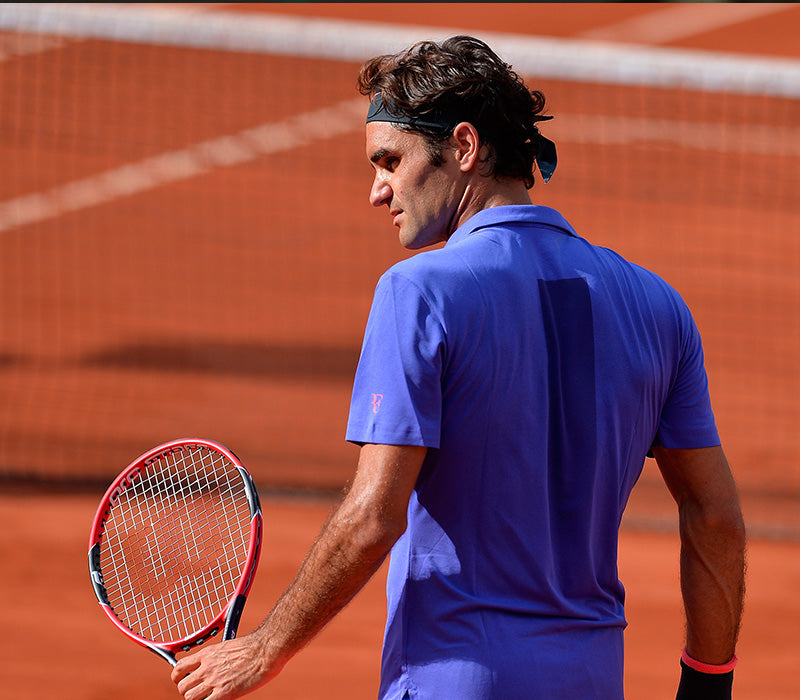 Roger Federer, back slightly turned to camera, holding his racket