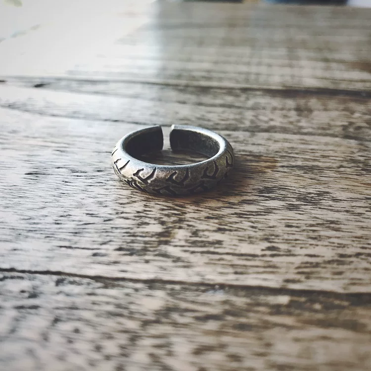 An antique silver adjustable motorcycle tire tread ring sitting on a rustic wooden table.
