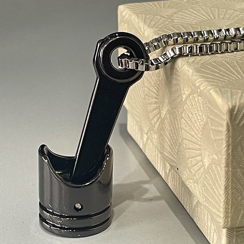 A sleek glossy black motorcycle piston pendant on a metallic silver chain close up view.