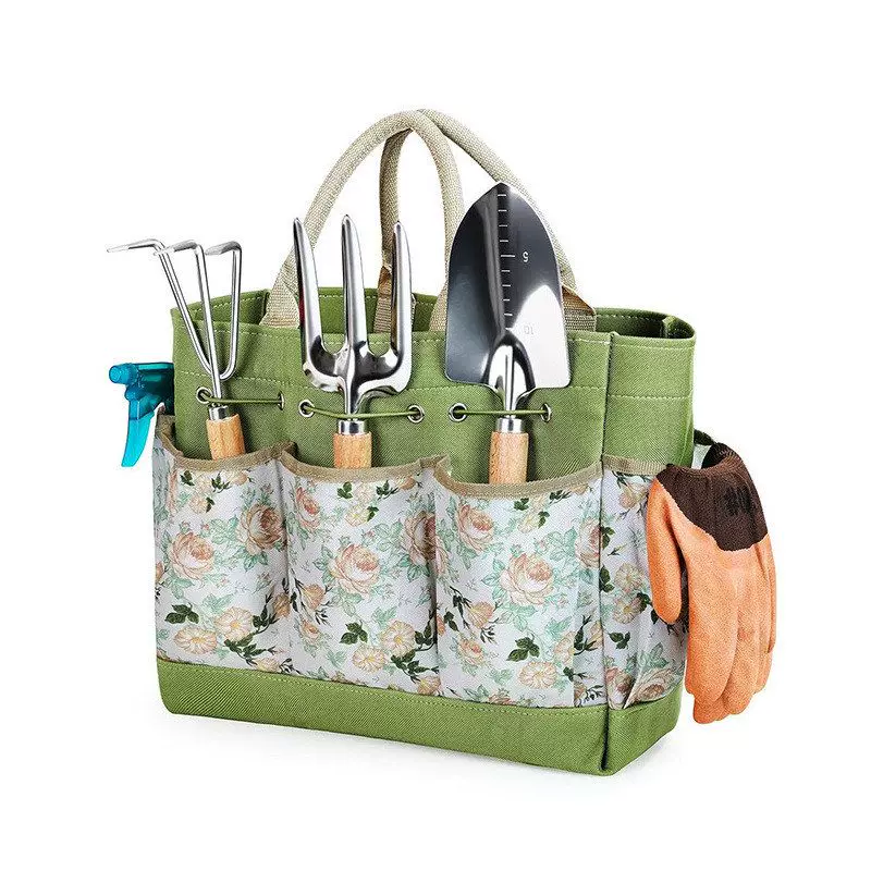A green and floral canvas gardening tote bag organized with hand tools and gloves hanging on the side.