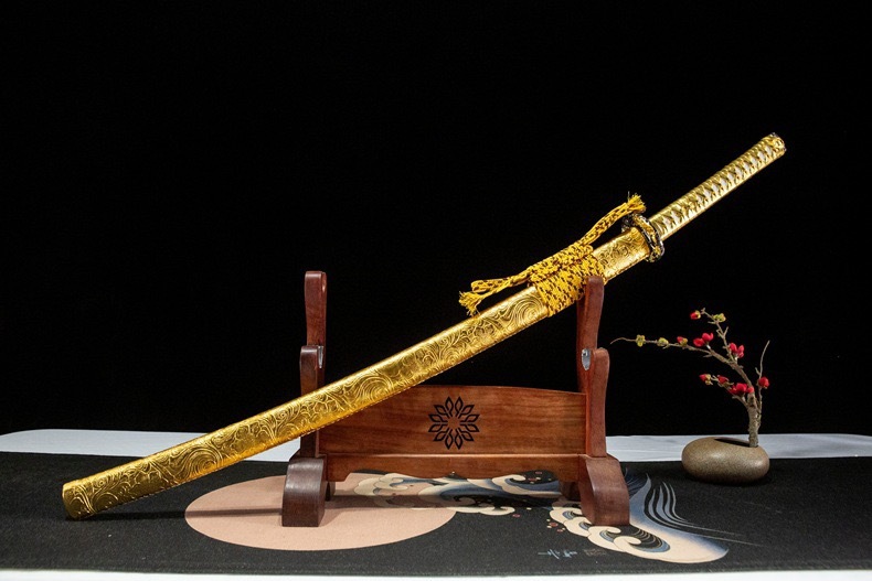 A stunning gold katana and scabbard angled dynamically on a wooden display stand.