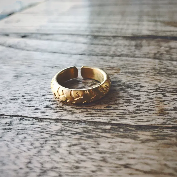 A gold-plated adjustable motorcycle tire tread band ring displayed on a wooden table.