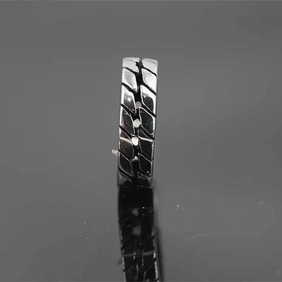 Close-up vertical view of the rugged tire tread pattern on a stainless steel biker ring, reflecting on a dark background.