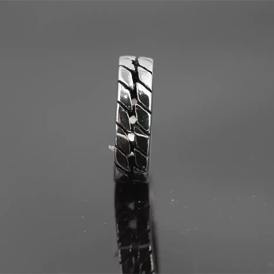 Close-up vertical view of the rugged tire tread pattern on a stainless steel biker ring, reflecting on a dark background.