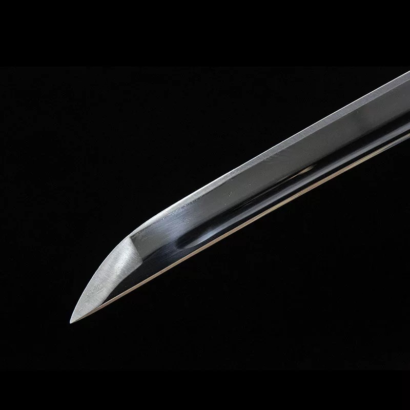 A clear close-up of the katana blade's point (kissaki) and visible hamon temper line, showing the edge geometry and the high-carbon steel quality.