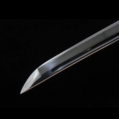 A clear close-up of the katana blade's point (kissaki) and visible hamon temper line, showing the edge geometry and the high-carbon steel quality.