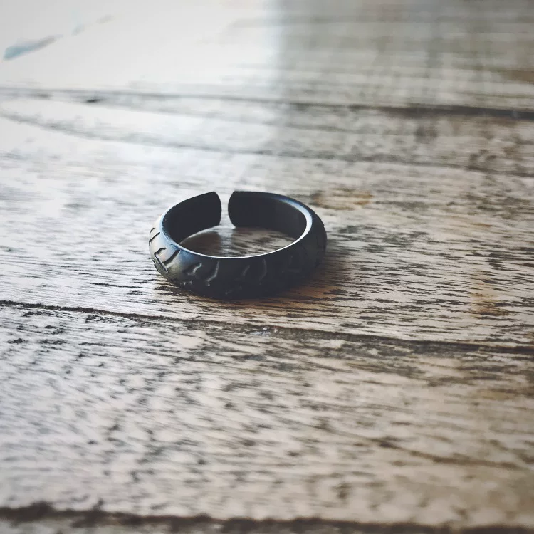 A matte black adjustable open-band motorcycle tire tread ring on a wooden surface.