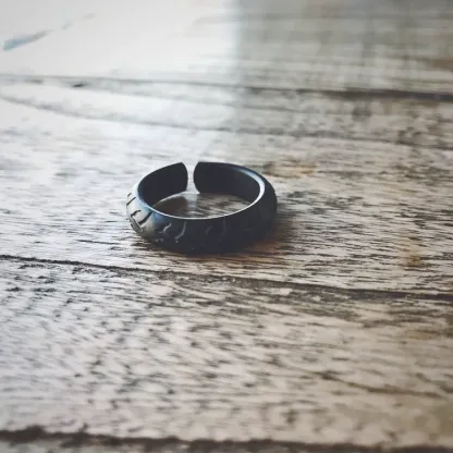 A matte black adjustable open-band motorcycle tire tread ring on a wooden surface.