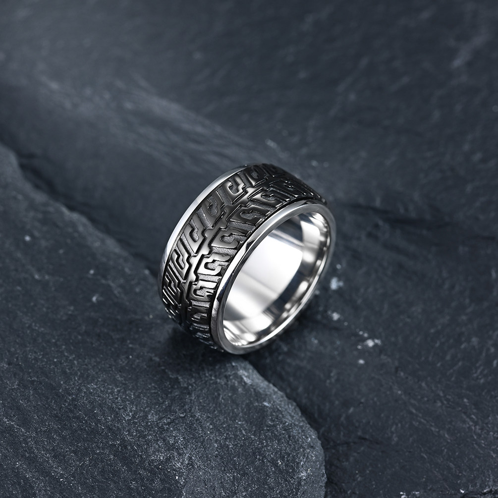 Mens silver stainless steel biker wedding band with tire track details resting on a textured dark rock.