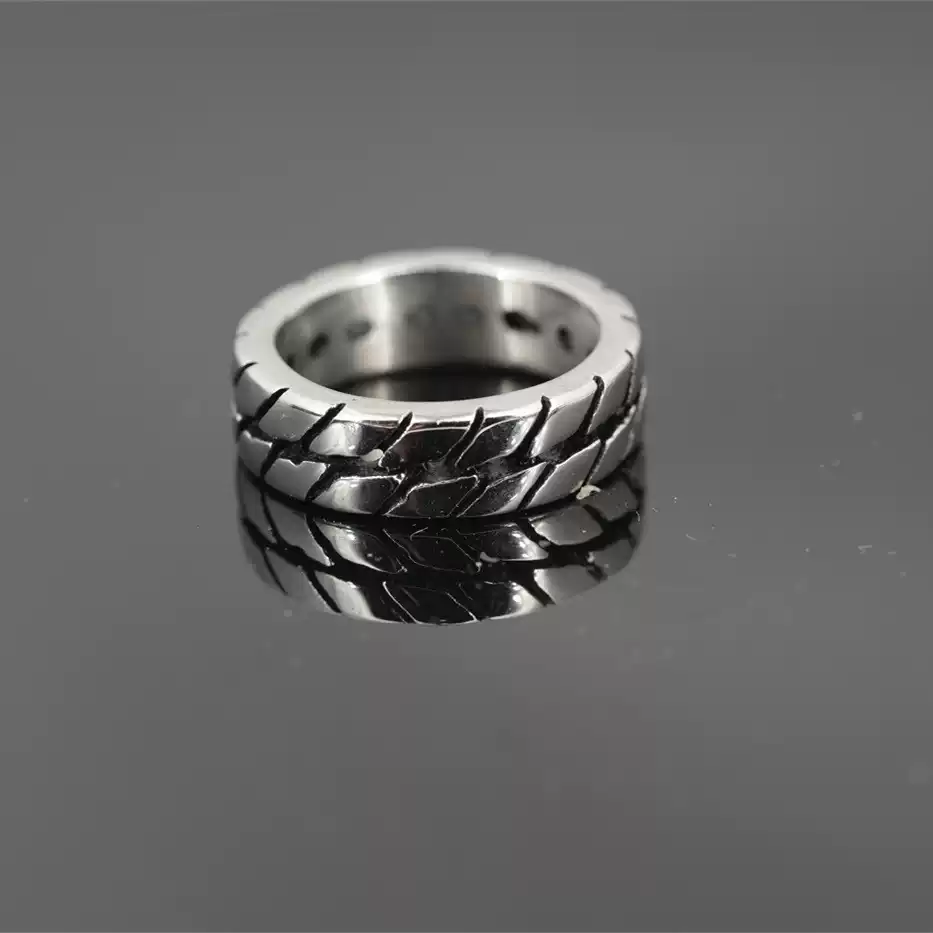 Men's motorcycle tire tread band ring made of durable stainless steel, resting on a dark reflective surface with a clear reflection.