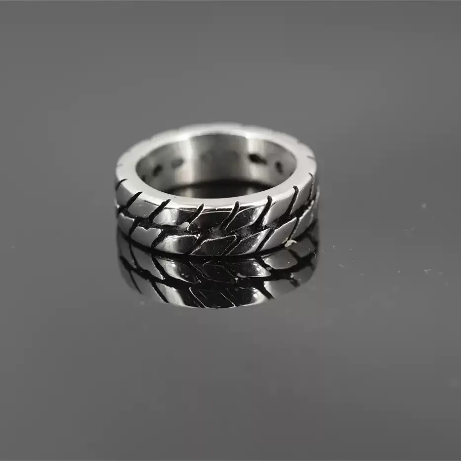 Men's motorcycle tire tread band ring made of durable stainless steel, resting on a dark reflective surface with a clear reflection.