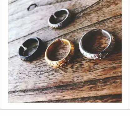 Four different colors of adjustable motorcycle tire tread rings including gold, black, silver, and antique silver arranged on a wooden background.