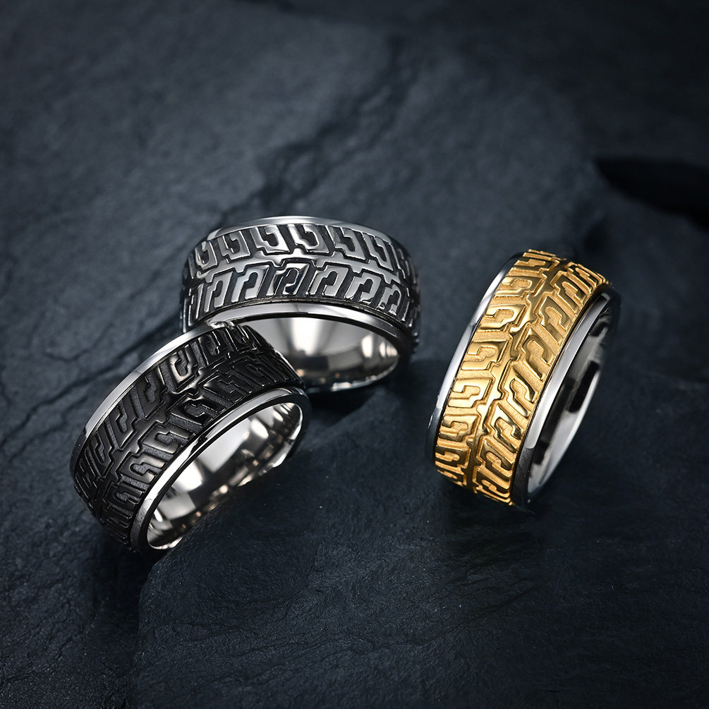 A collection of three motorcycle tire tread spinner rings in silver, black, and gold colors on a dark stone background.