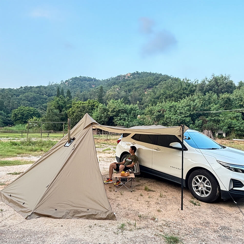 A camper sitting in a chair next to the pyramid tent, highlighting the easy-to-use car awning feature.