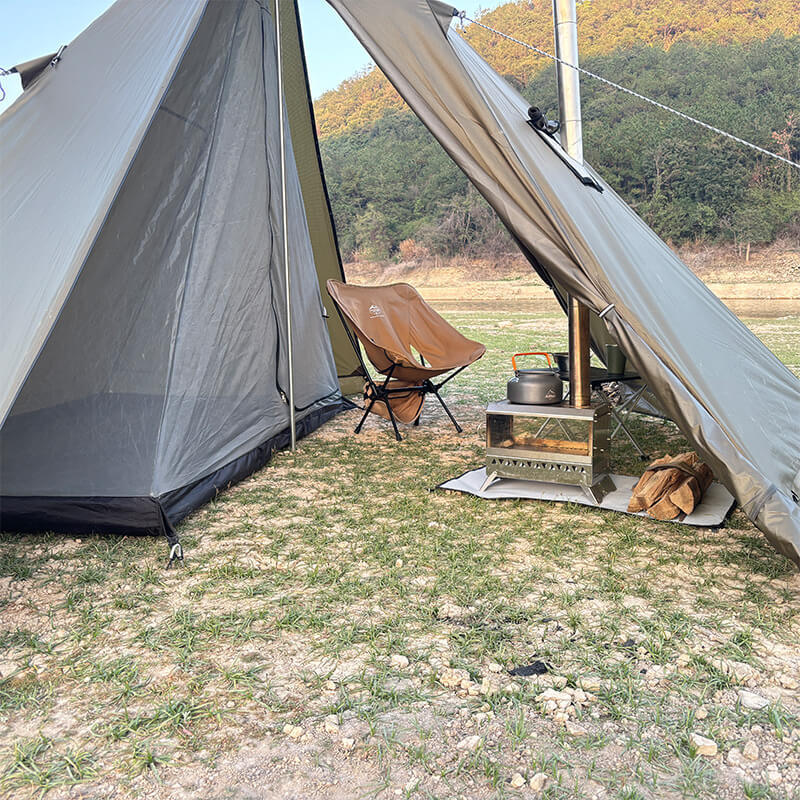A tan pyramid hot tent set up with a camping stove and chair, showing a comfortable and functional camp site.