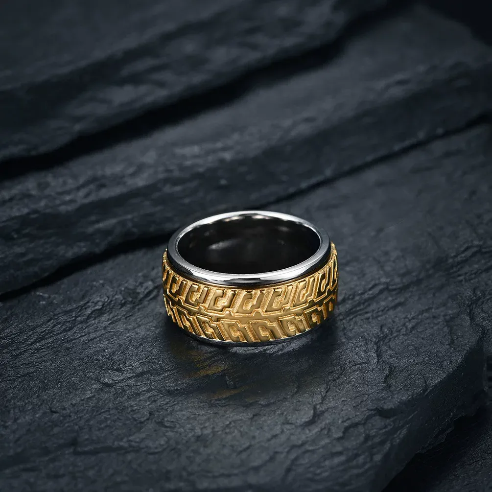 A two-tone gold and silver stainless steel motorcycle tire tread spinner ring flat on a dark rock background.
