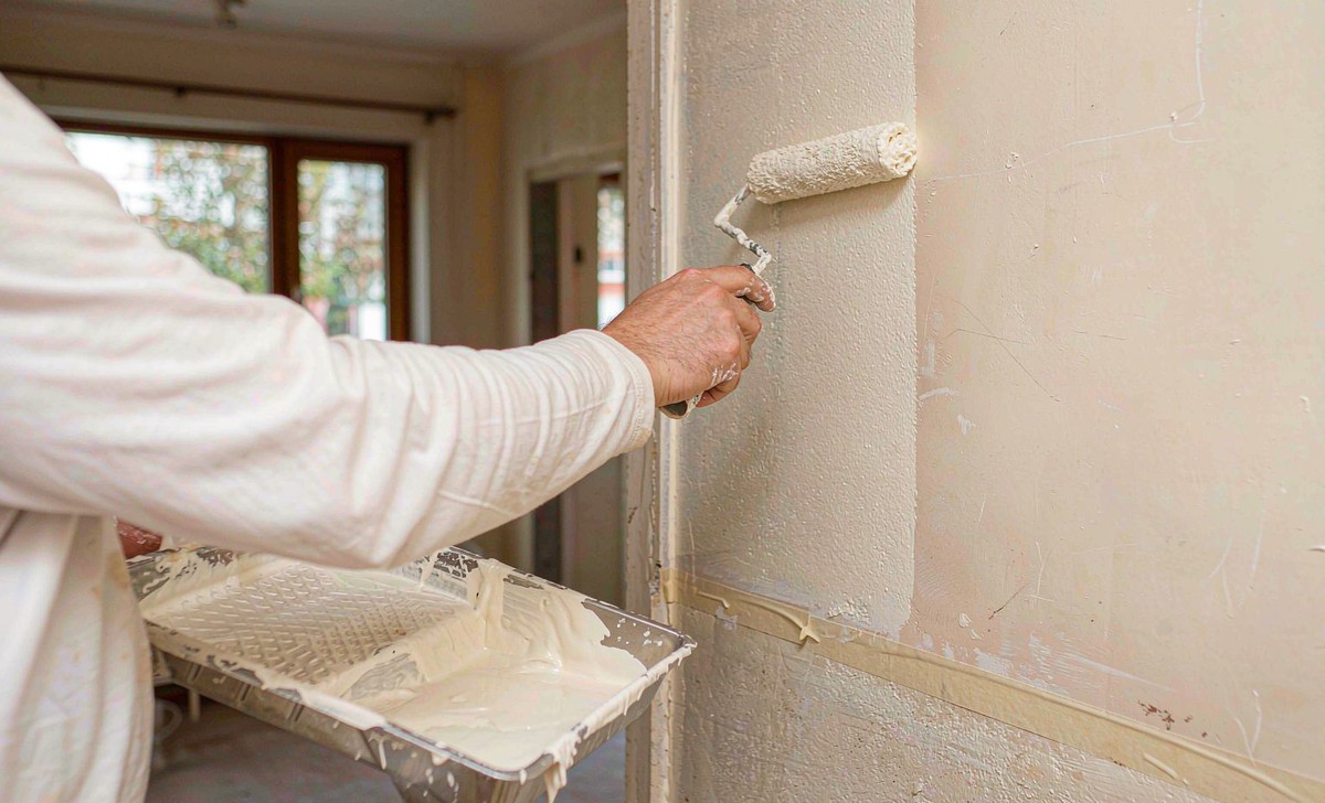 Painter rolling off-white emulsion onto a freshly plastered wall
