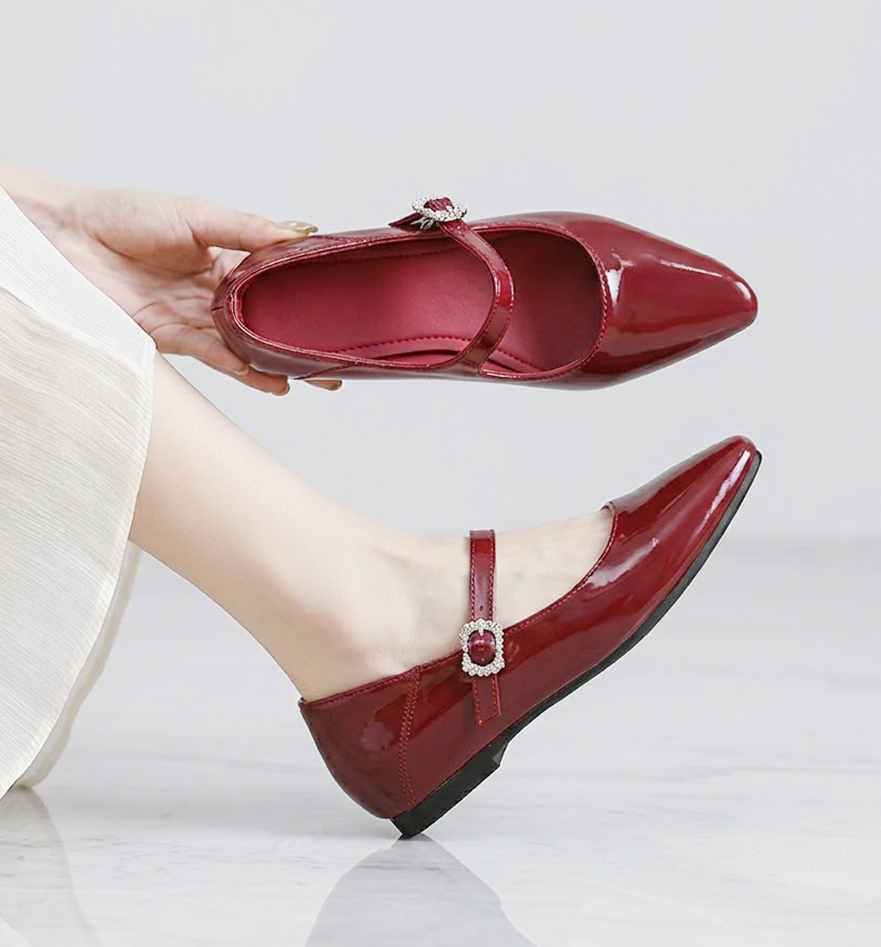 赤いマリージェーンパンプスを手に持った写真。キラキラ光るバックルのデザインと、ポインテッドトゥのきれいなシルエットが特徴。4.5cmインヒール内蔵。