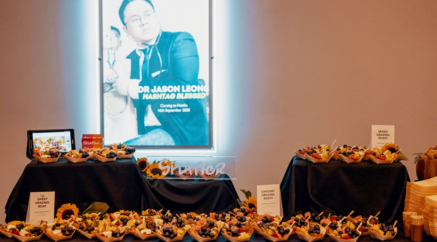 Grazing table spread with a poster of Dr Jason Leong's Netflix comedy special show, Hashtag Blessed, at the back. 