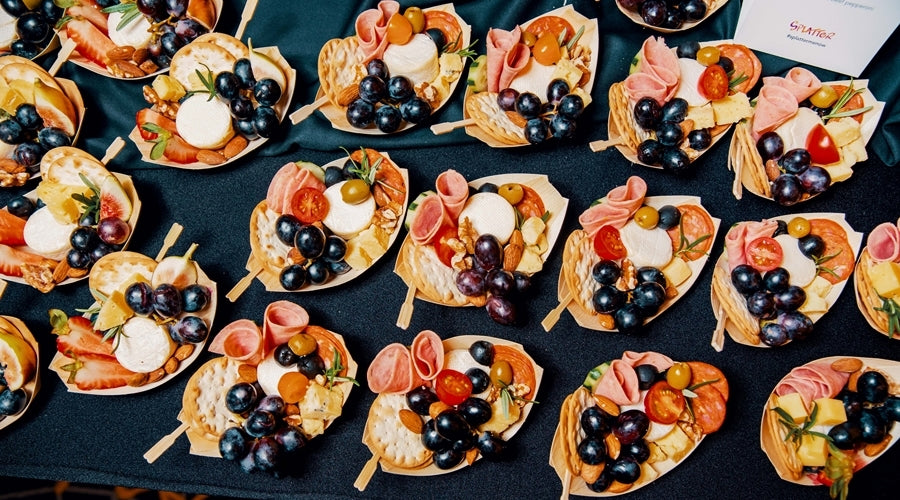 Small grazing boats filled with cheeses, charcuterie, fruits, and crackers lined on a table. 