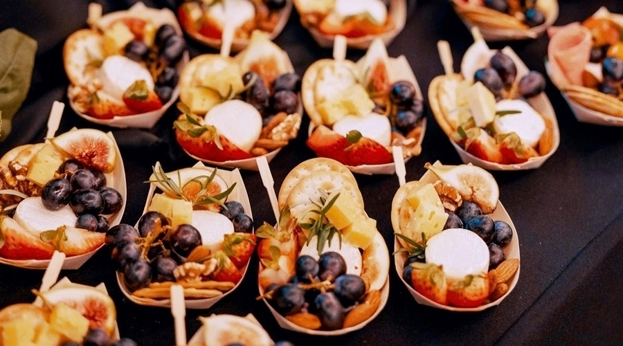 Grazing boats filled with cheeses, charcuterie, fruits, crackers lined on a table