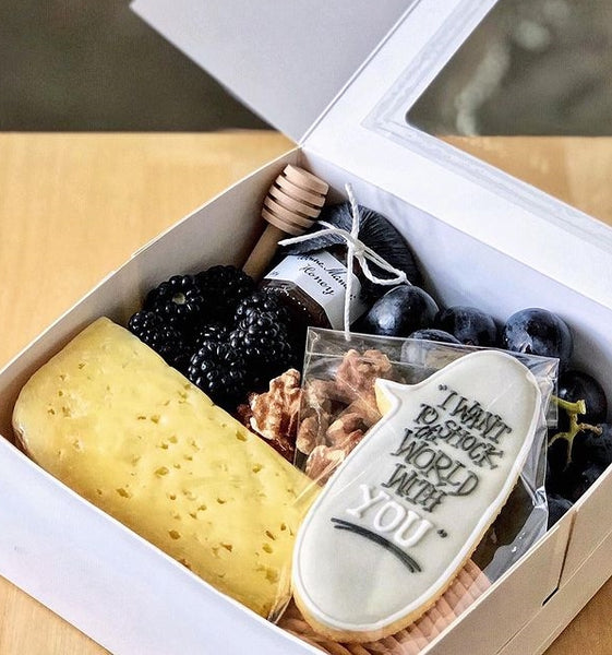 White gift box filled with artisanal cheese, designer cookie, and other accompaniments in black and grey colour scheme. 