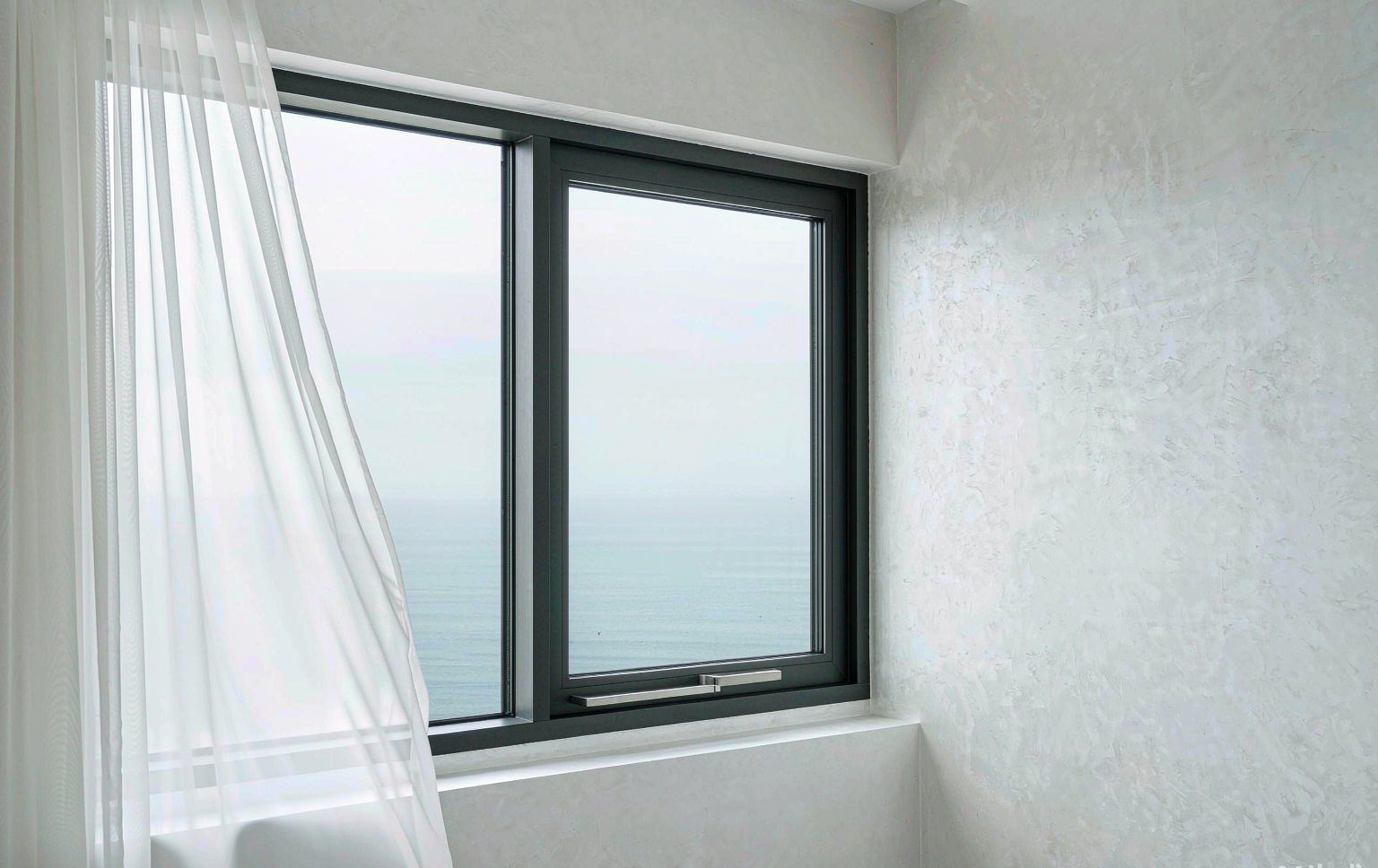 A slim matte black aluminium window installed in a bright white room