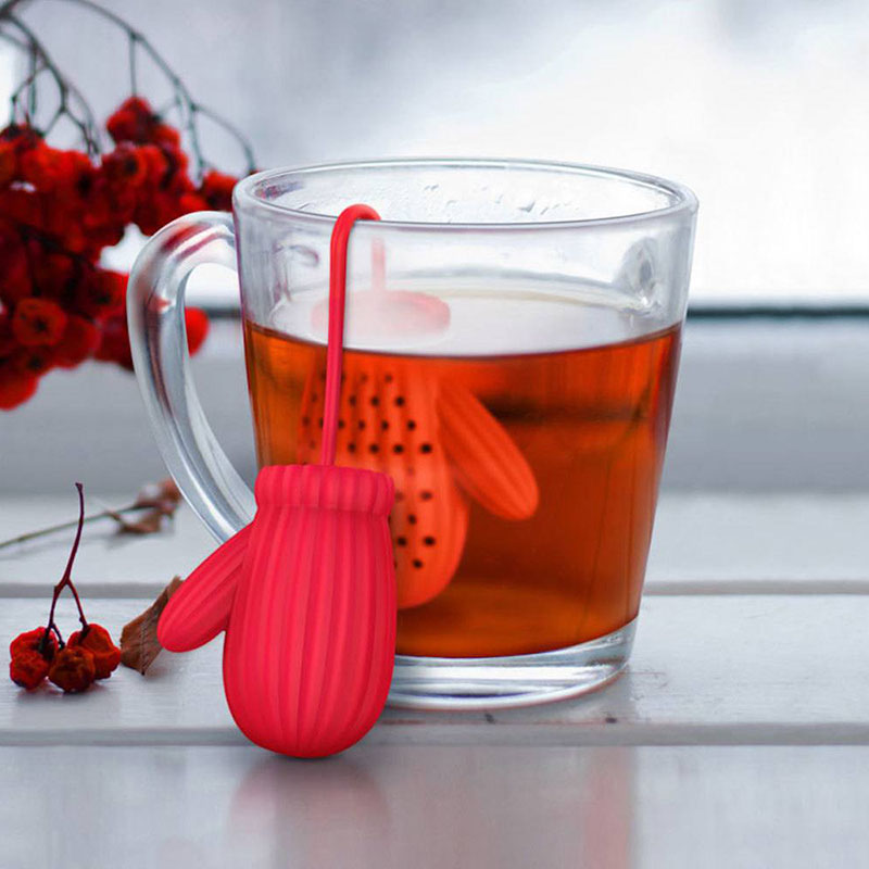 red winter knitted mitten silicone tea infuser inside transparent glass mug winter scene white wood table