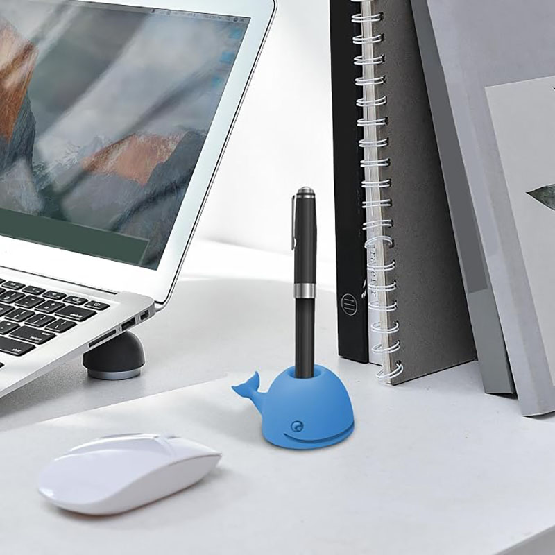 light blue smiling whale silicone pen holder with black pen on white office desk scene