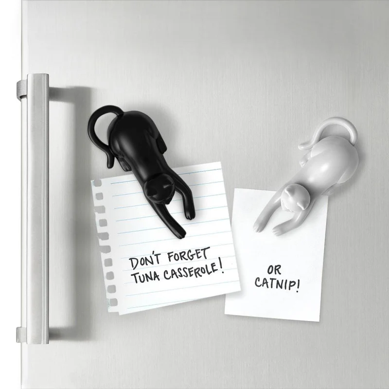 black and white hanging stretch cat plastic fridge magnet holding note on refrigerator white background scene
