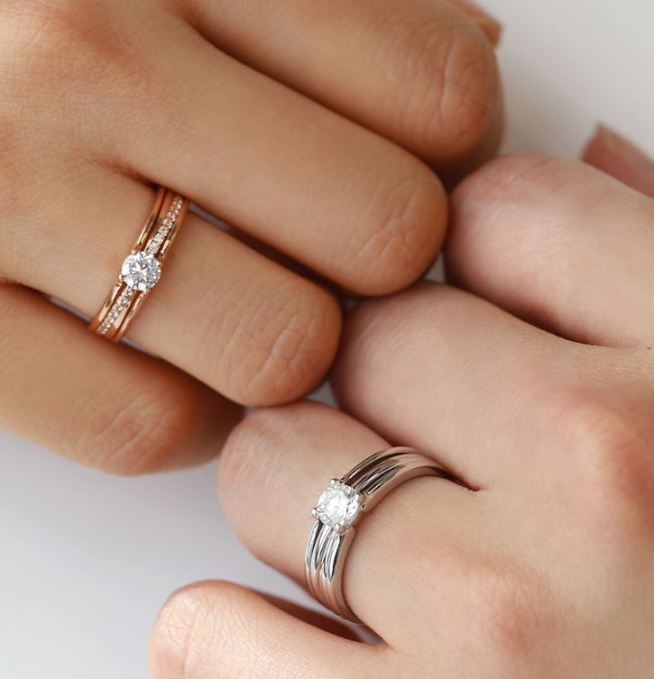 男女模特兒佩戴 DIABOND 天然鑽石結婚對戒牽手近拍。女方佩戴玫瑰金色多層次線條戒指，鑲嵌 0.4ct 主鑽；男方佩戴銀白色同款寬版對戒，鑲嵌 0.5ct 主鑽，盡顯立體層次與份量感。