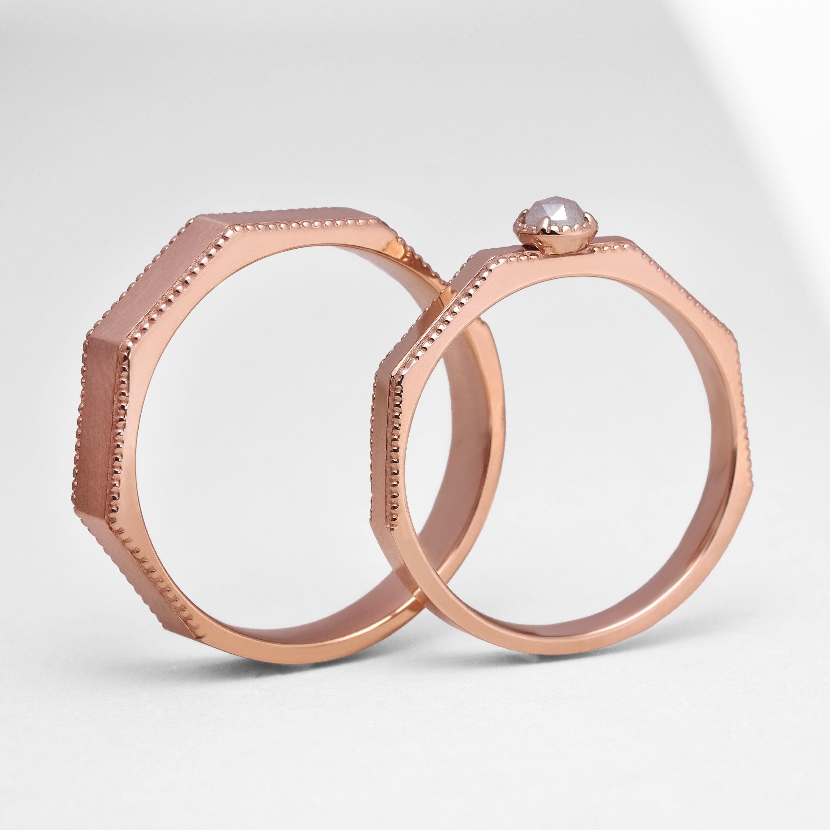 一對玫瑰金色八角形復古結婚對戒直立近拍。清晰可見戒指邊緣細膩的滾珠邊打磨工藝。左側女戒鑲嵌著未經打磨切割的 0.1ct 綠色毛胚天然鑽石，呈現獨特原始質地；右側為簡約俐落的男戒。