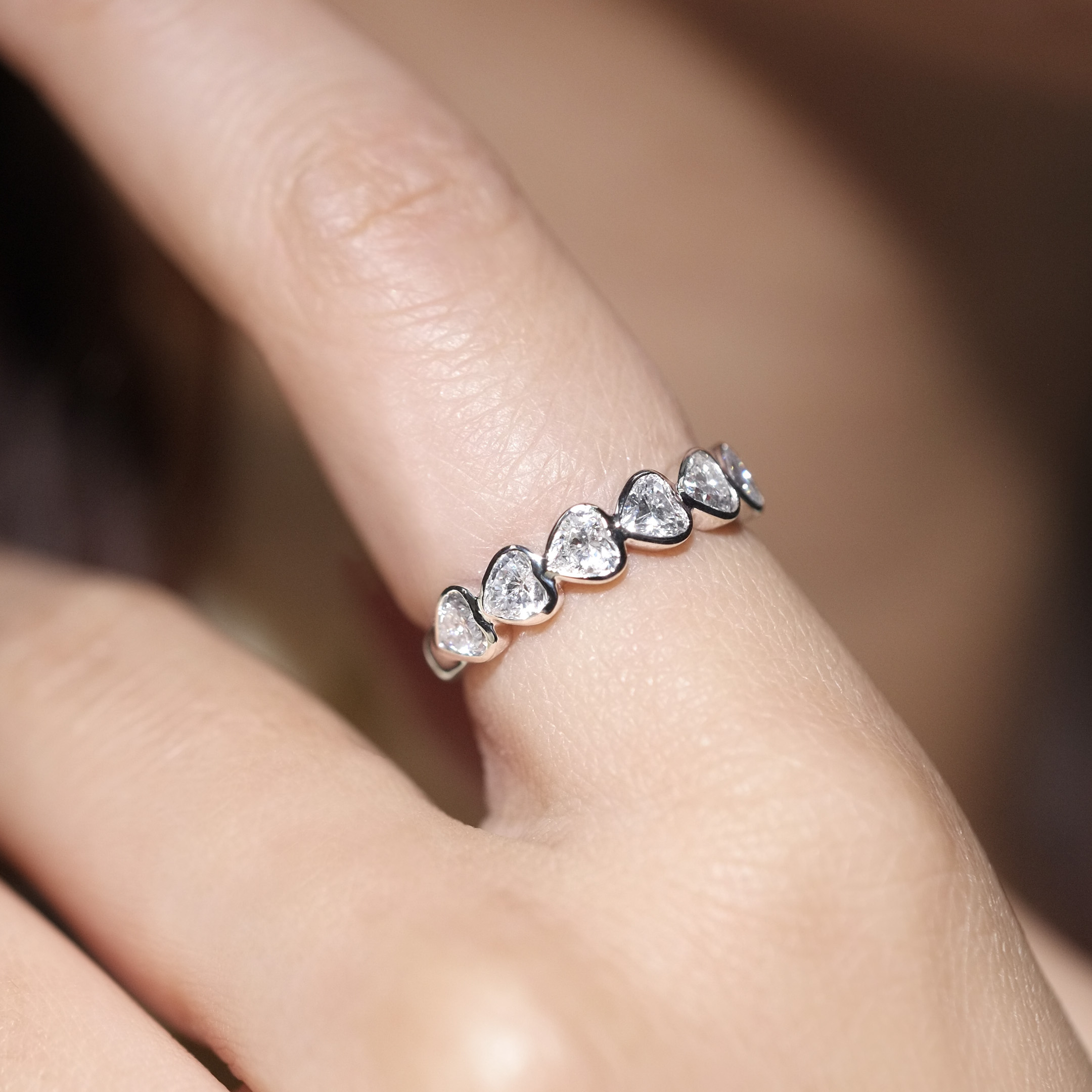 Woman wearing heart shape bezel set diamond eternity ring on finger, snag-free design