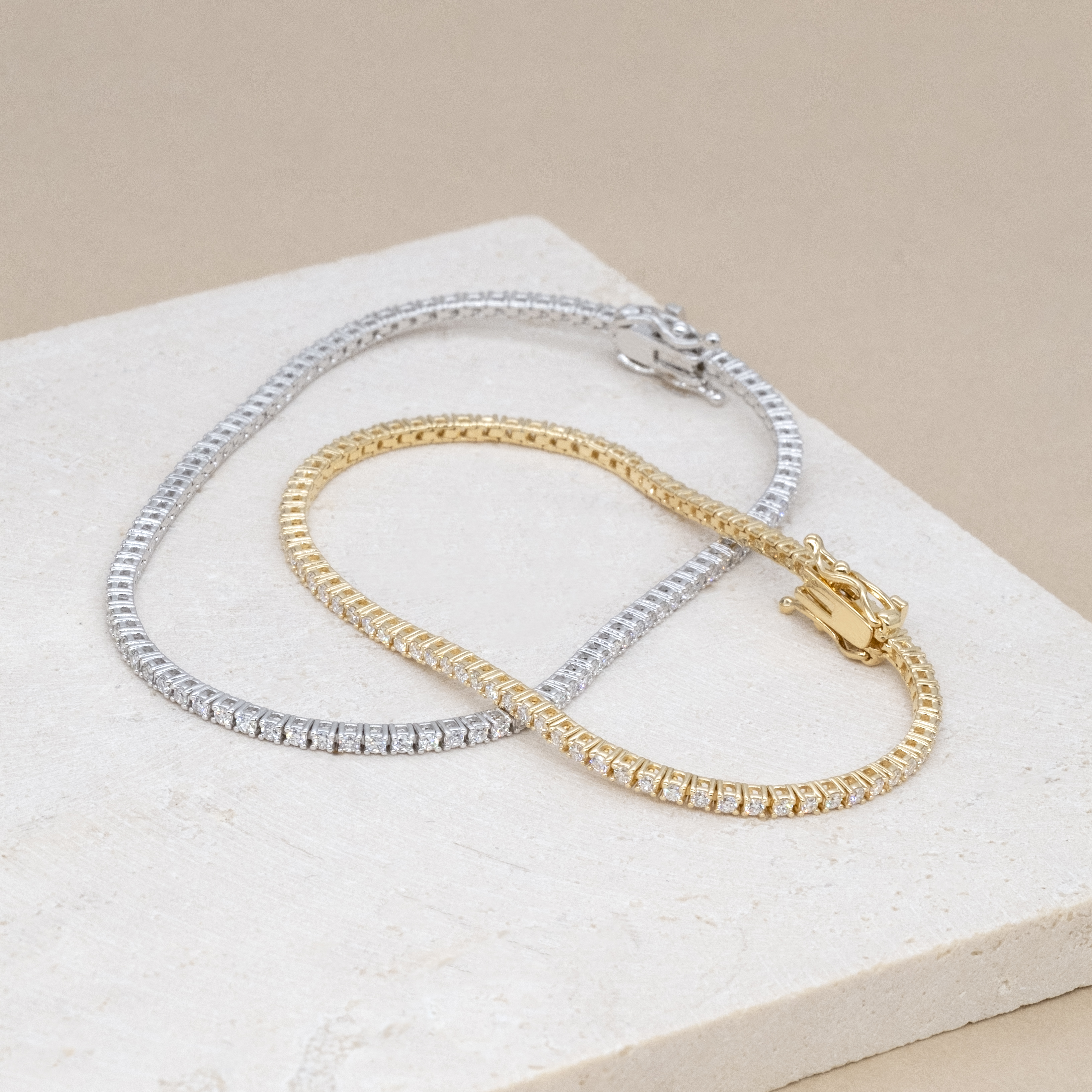 18K yellow gold and 18K white gold micro tennis bracelets on stone texture background