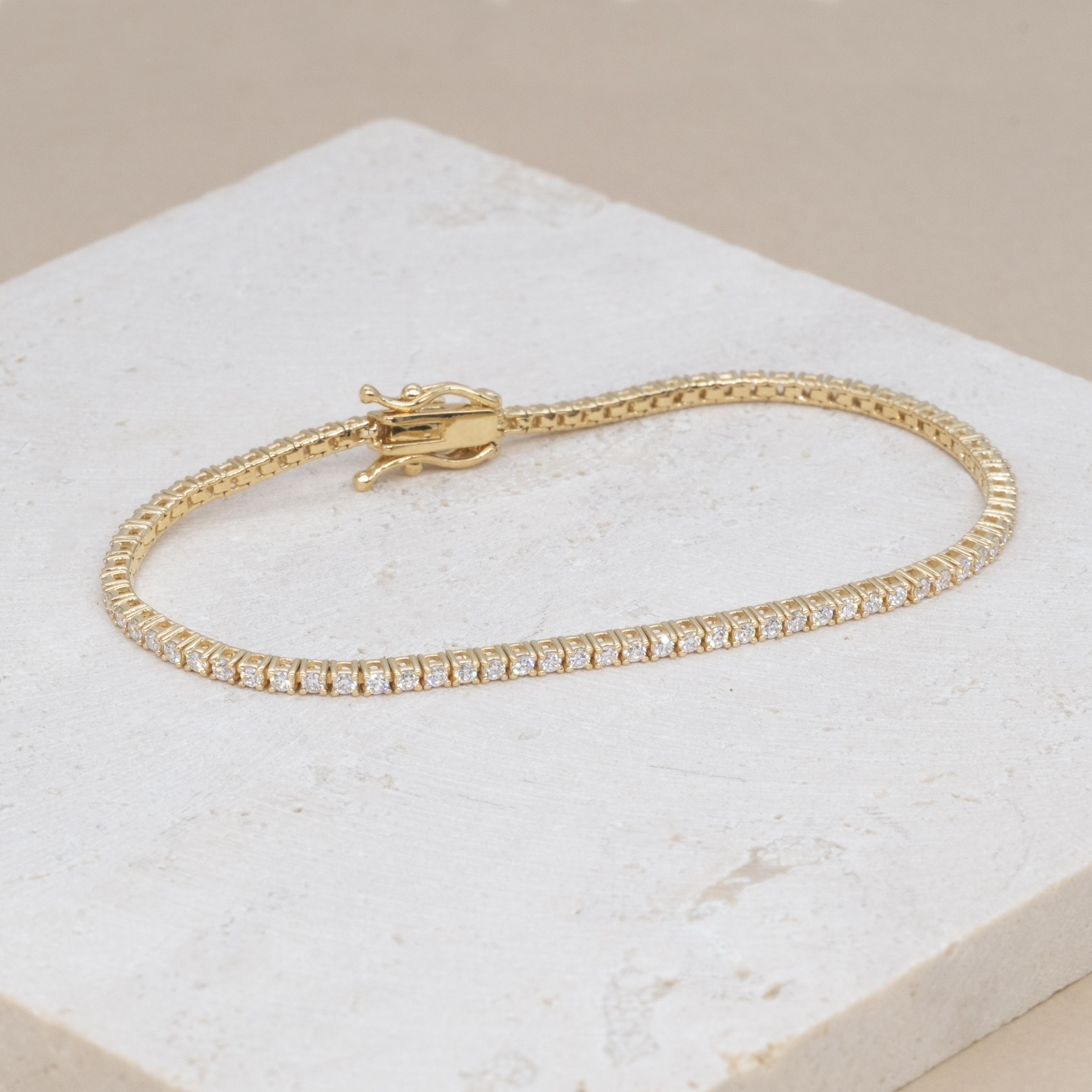 18K yellow gold micro tennis bracelets on stone texture background