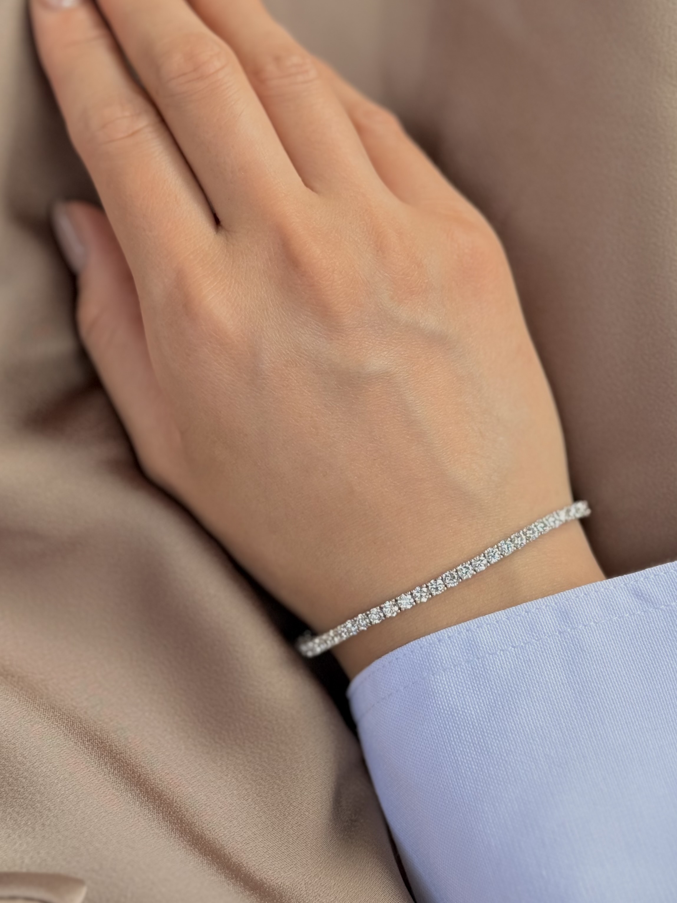 Woman wearing 5.59ct luxury 3mm diamond tennis bracelet in white gold on silk background.