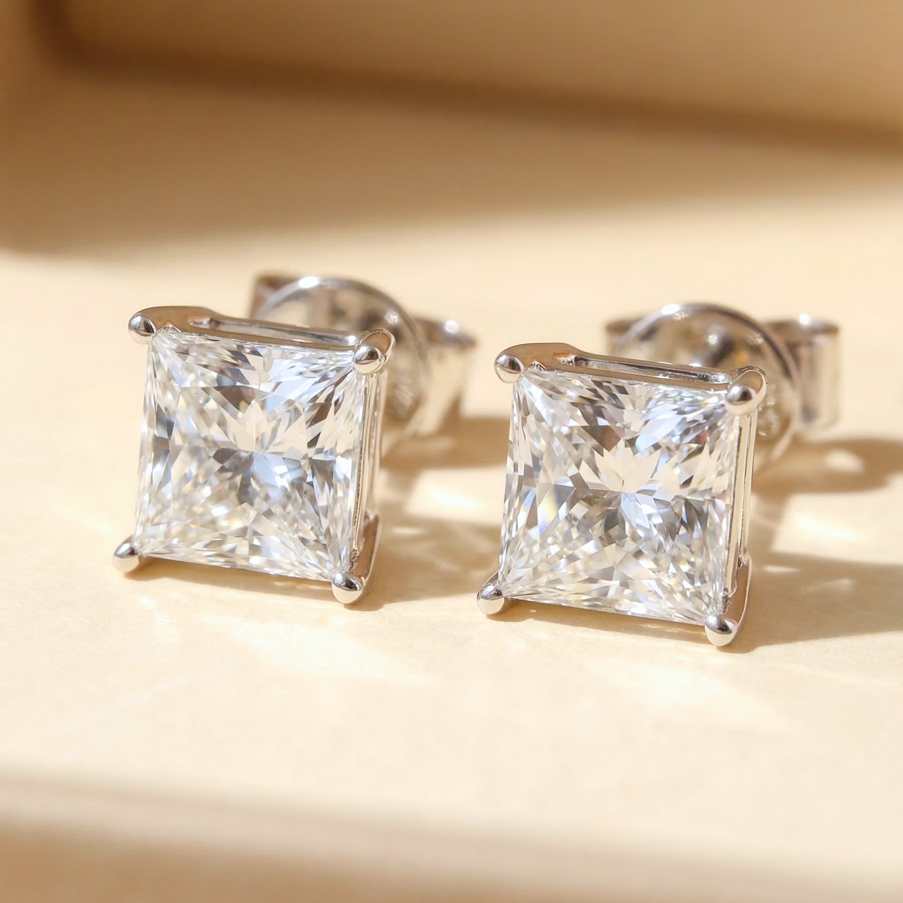 一對總重 2 克拉的公主方形培育鑽石單鑽耳環平放特寫。採用 18K 白金打造專屬的 V 型四爪鑲嵌（V-Prong Setting），完美保護鑽石四個銳角，同時將每邊 1 克拉（D/E 色、VS 淨度）公主方切割鑽石的十字星火彩與幾何線條發揮到極致。附雙 IGI 證書。