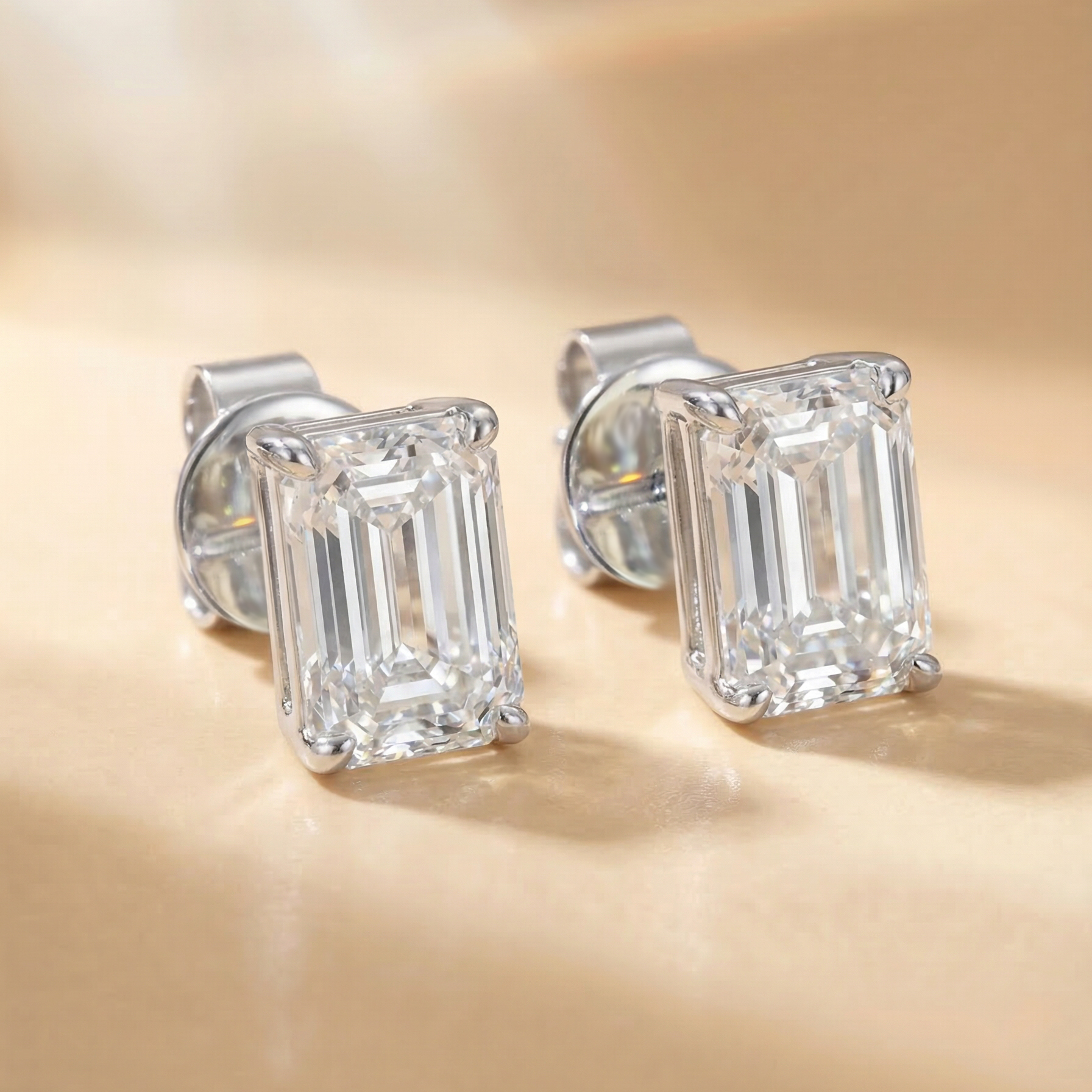一對總重 2 克拉的祖母綠形培育鑽石單鑽耳環平放特寫。採用 18K 白金四爪鑲嵌，完美展現每邊 1 克拉（D/E 色、VS 淨度）祖母綠切割 (Emerald Cut) 獨有的階梯式刻面 (Step Cut)。其長方形輪廓散發著極致的清透感與復古高級的幾何美學。