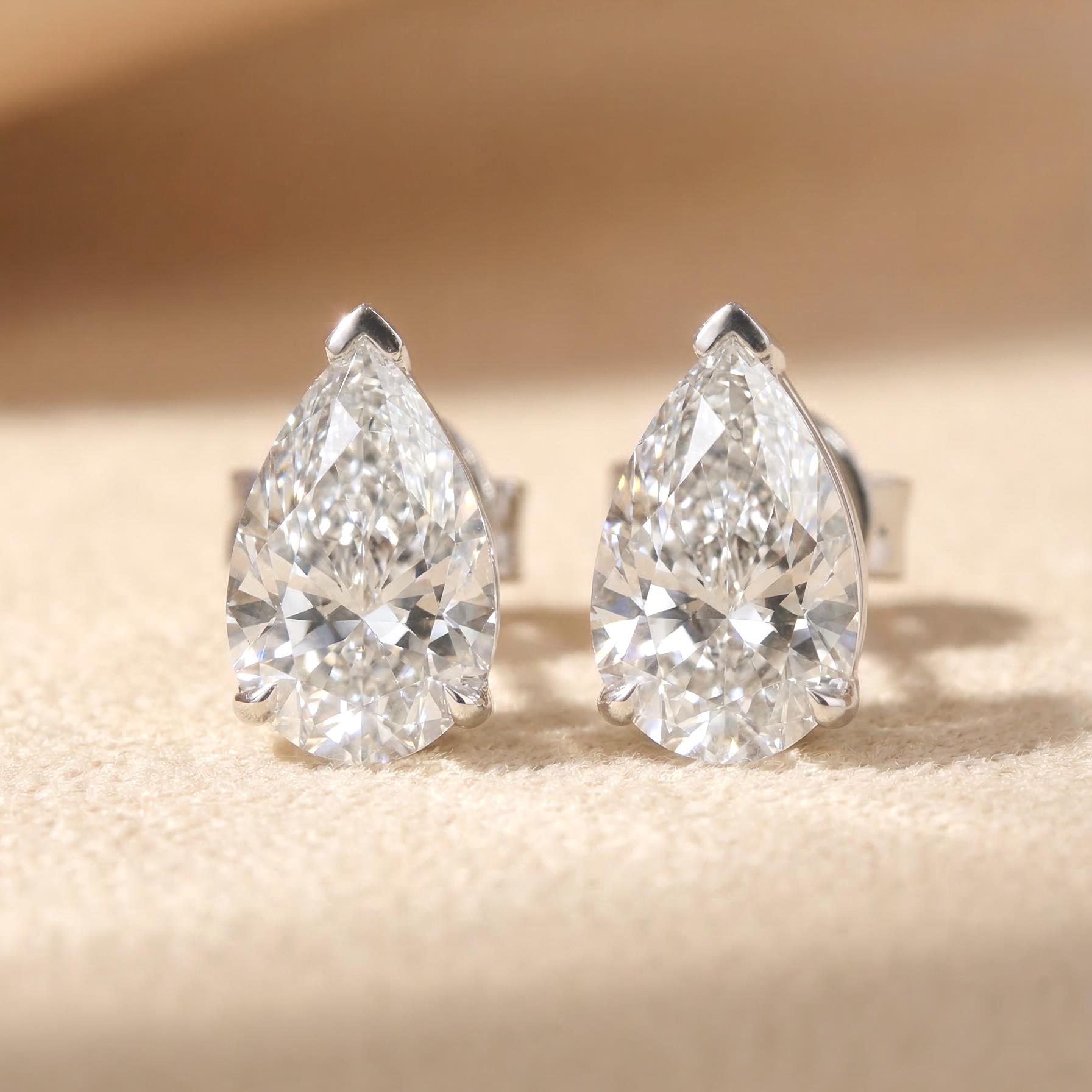 一對總重 2 克拉的水滴形培育鑽石單鑽耳環平放特寫。採用 18K 白金經典三爪鑲嵌（頂端 V 型鑲爪保護尖端），完美呈現每邊 1 克拉（D/E 色、VS 淨度）梨形切割鑽石的飽滿輪廓與極致火彩。附有雙 IGI 國際證書保證。