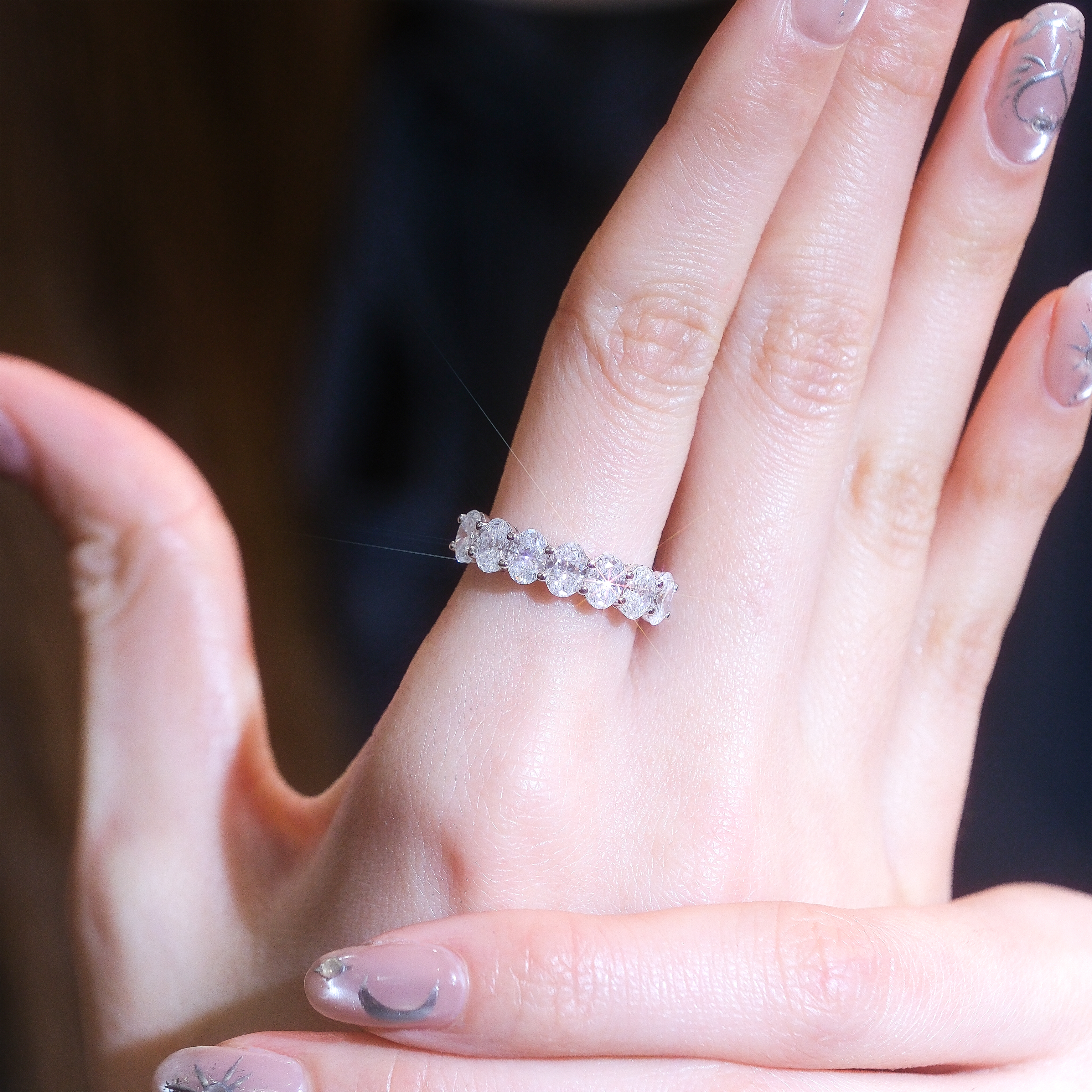 模特兒佩戴 2.1 克拉橢圓形排鑽戒指的手部特寫。七顆橢圓形培育鑽石在指間形成一道閃耀的弧線,修長的鑽石形狀能有效修飾手指線條,讓雙手更顯纖細。非常適合作為結婚對戒、疊戴戒指或週年紀念禮物。