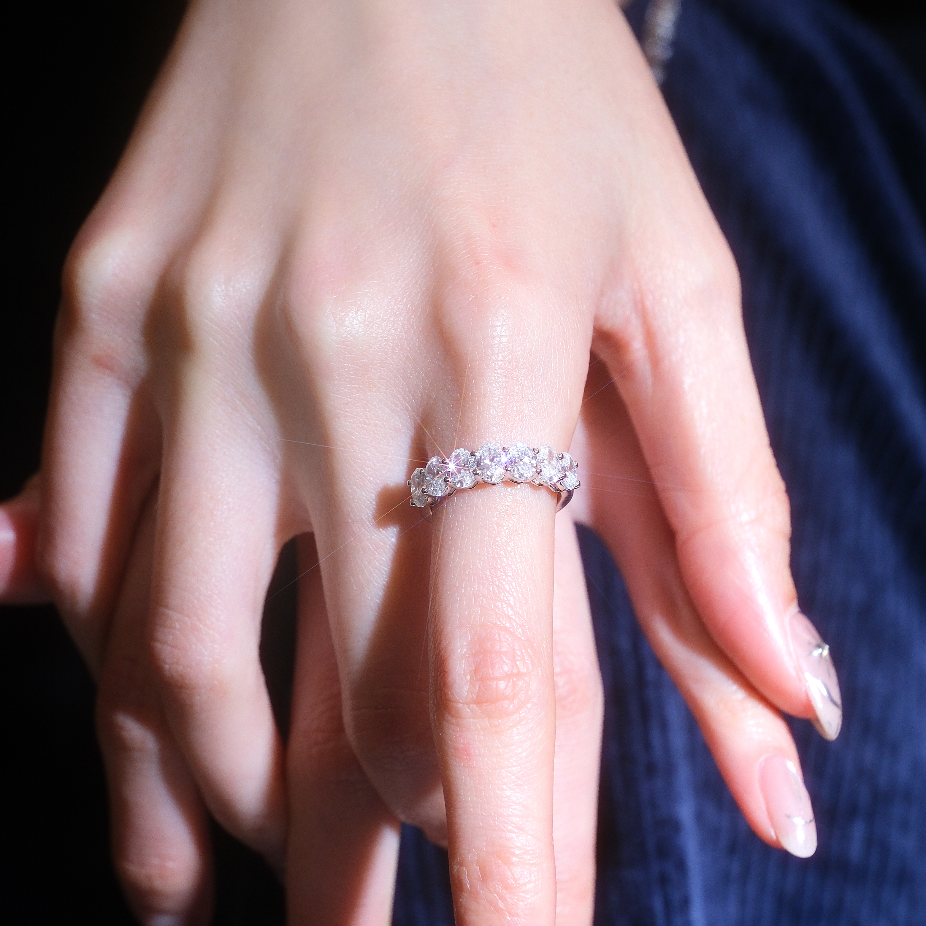 模特兒佩戴 2.1 克拉橢圓形排鑽戒指的手部特寫。七顆橢圓形培育鑽石在指間形成一道閃耀的弧線,修長的鑽石形狀能有效修飾手指線條,讓雙手更顯纖細。非常適合作為結婚對戒、疊戴戒指或週年紀念禮物。