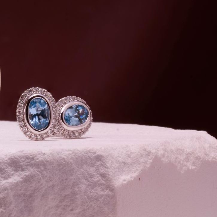 Oval aquamarine colored blue spinel stud earrings with diamond halo in 18k white gold.