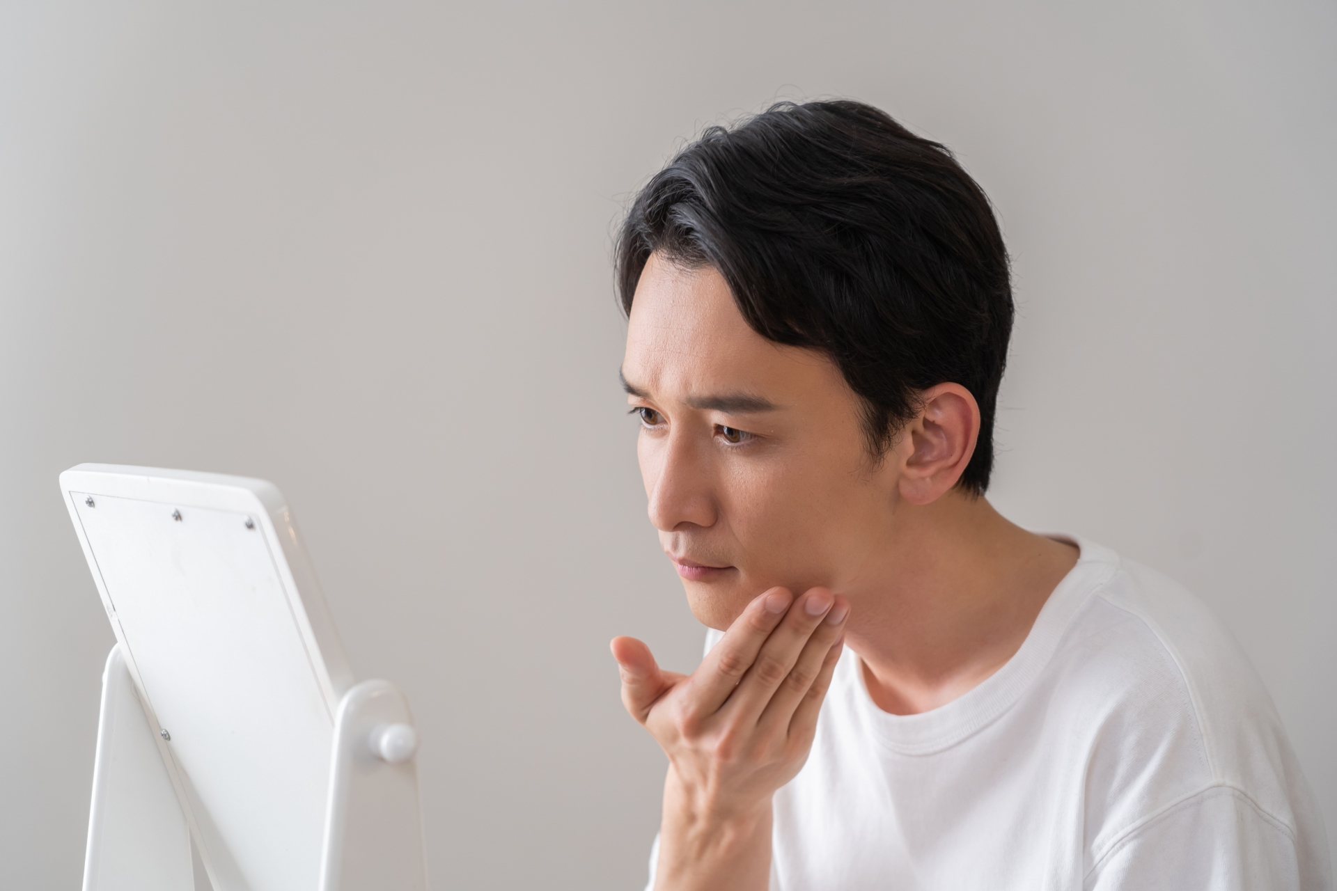 鏡を見ながら肌の艶を気にする男性