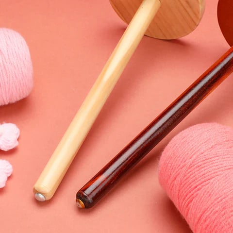 The Levitating Premium Yarn Holder and balls of pink yarn, perfect for seamless knitting, are displayed on a peach-colored surface.