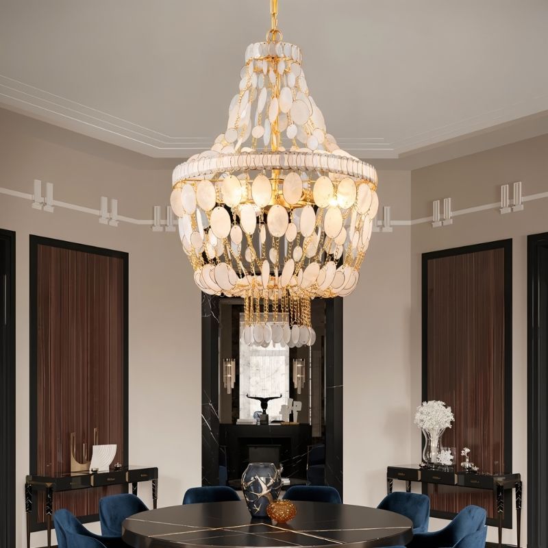 "Tiered chandelier with cascading natural shell elements and gold frame, illuminating a dining room with a round table."